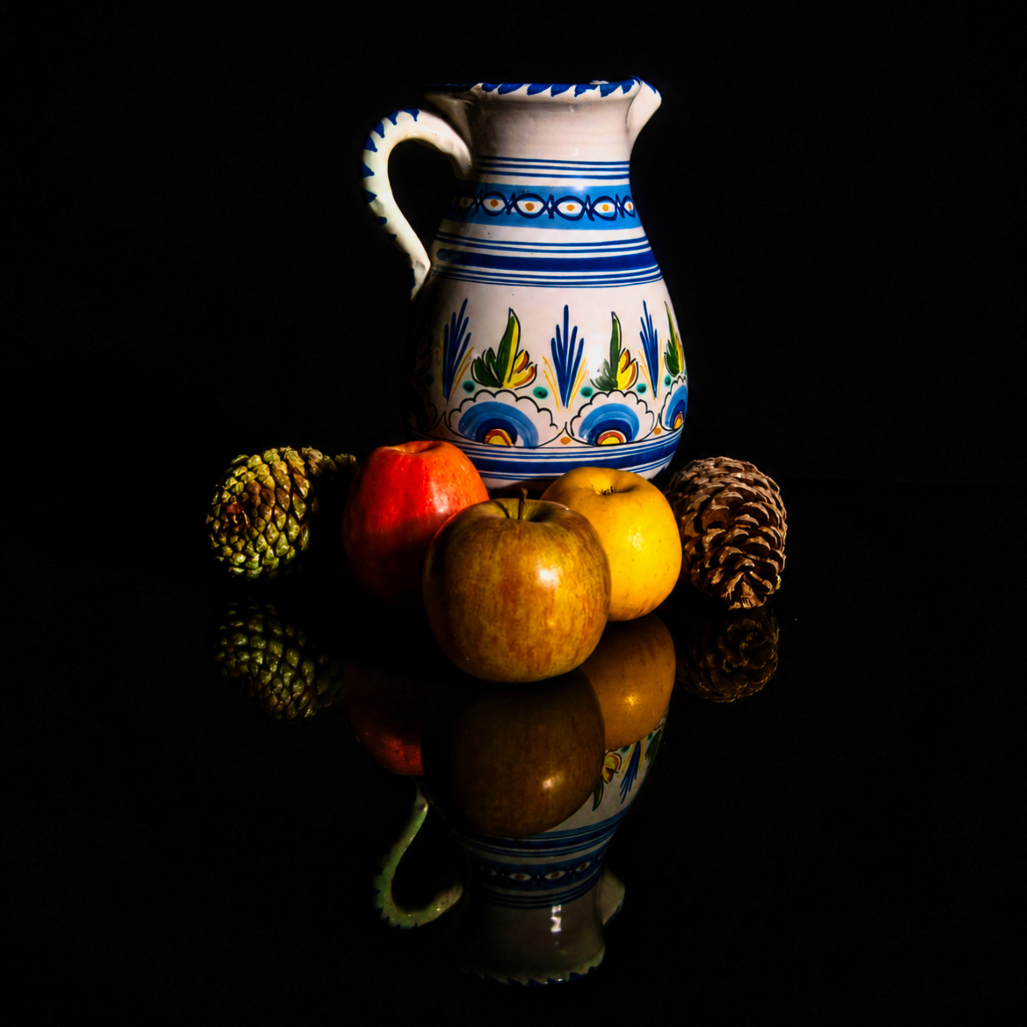 Cruche décorée, pommes et pommes de pin sur fond noir